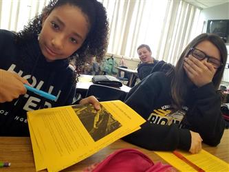 students at desks, pointing at paper