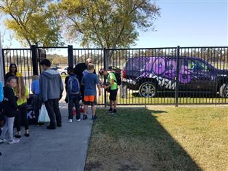 students lined up outside next to car with 102.5fm sign