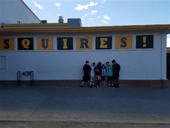 students posing next to squires banner
