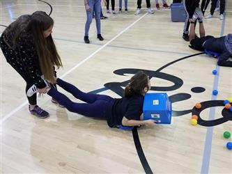 student on stomach collecting balls with bucket